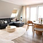 Wohn- und Essbereich mit Sofa, Tisch und Stühlen. Holzboden und große Fenster.