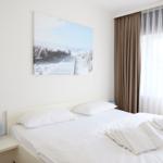 A bed with white linens and towels. Wall art shows a beach. Curtains are brown and white.