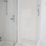 Shower with glass enclosure and shower head, white tiles and mirror