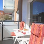 Terrace with table, two chairs, and orange cushions. Breakfast set and view of buildings.