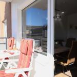 Terrace with table and chairs with orange cushions. Dining room visible through glass door.