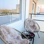 Balcony with two wicker chairs, fur throws, small table, and glasses. View of buildings and trees.