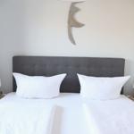 Ein Bett mit weißen Kissen und einer grauen Kopfseite. Zwei Nachttische mit Lampen.