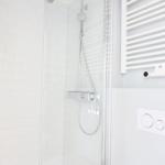 Dusche mit Glaswand, weißen Fliesen und modernem Duschsystem.
