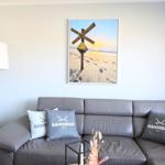 Grauer Sofa mit Kissen und Wandbild mit Strandmotiv.