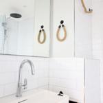 Badezimmer mit weißer Fliesenwand, Spiegel und Seilhaken.