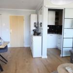Wohnung mit Essbereich, Küche und Wohnzimmer. Holzboden und weiße Möbel.