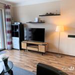 Wohnzimmer mit TV, Holzboden und Balkontür.