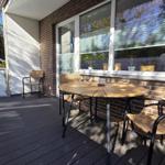 Deck with wooden table and chairs, adjacent to living area with window.