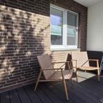 Terrace with two chairs, wooden decking, and brick wall. Window and railing are visible.
