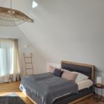 Schlafzimmer mit Dachschrägen, Holzboden und Bett mit grauer Bettdecke.