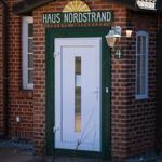 Entrance door with sign Haus Nordstrand on a red brick house.