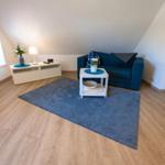 A living room with blue sofa, white table, and blue rug on wooden floor.