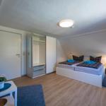Bedroom with double bed, wardrobe, and TV. Wooden floor and blue rugs.