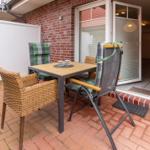 Terrace with table and chairs, glass door to house, red brick paving.