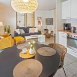 Dining area with round table and chairs, kitchen with white cabinets and living room with sofa and yellow seating.