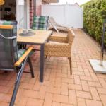Terrace with table, chairs, and grill area beside hedge.