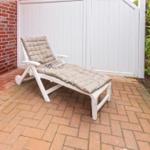 White lounge chair with cushion on terrace next to wall and hedge.