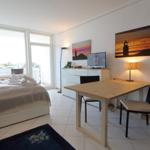 Bedroom with bed, desk, TV, and balcony view.