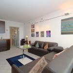 Living room with sofa, coffee table, and kitchen area. Wall art and floor lamp visible.