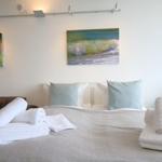 A bed with white pillows and folded towels. Two pictures hang on the wall.