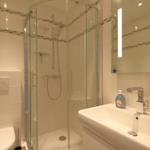 Bathroom with shower, sink and toilet. Tiles and mirror are visible.