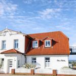 House with red roof and white facade, surrounded by a white fence with sea view.
