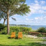 Two wooden chairs under a tree with a view of the sea and a harbor.