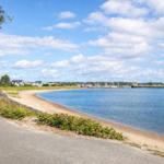Path along the beach with view of harbor and houses.