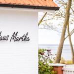 Haus Martha with white wall and red roof, view of water and trees.