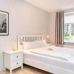 A bedroom with a white bed, nightstands, and a window with curtains.