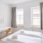 Room with two beds, desk, and two windows with blinds and striped curtains.