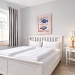A bedroom with a white bed, fish artwork on the wall, and a nightstand with a lamp.