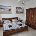 Schlafzimmer mit Holzbett, Kleiderschrank und Strandbildern an der Wand.