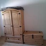 Wooden wardrobe with two doors and drawer, next to wooden chest with lid.