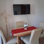 Dining table with four chairs, red tablecloth, and flowers. Wall-mounted TV and floor lamp.