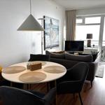 Rundes Esszimmer mit Tisch, Stühlen und Wandbild. Wohnbereich mit Sofa und TV. Balkon mit Sicht auf Stadt.