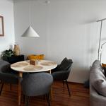 Rundtisch mit vier Stühlen, Sofa mit Kissen und Stehlampe im Wohnbereich.