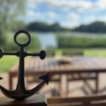 A small anchor sits on a wooden block. In the background, a patio with a table overlooks water and greenery.