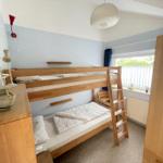 A bedroom with a wooden bunk bed, a window, and a wardrobe.