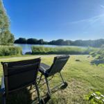 Two lounge chairs on a lawn with a view of a lake and trees.