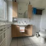Bathroom with sink, toilet, and window. Wooden cabinets and tiles.