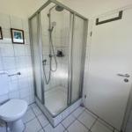 Bathroom with shower, toilet, and white tiles.