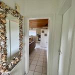 Mirror with shell frame in hallway. View into kitchen and living area with wooden ceiling.