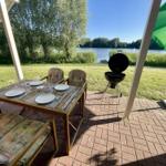 Patio with table, chairs, grill, and green umbrella by the lake.