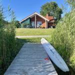 A surfboard rests on a wooden path leading to a house with a garden.