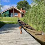 A canoe sits on a wooden dock in front of a house with a red roof.