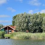 A house by the water with trees and tall grass in the foreground.