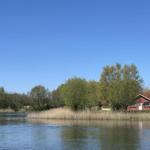Red house by the lake with trees and clear sky.