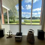 View of a lake through large windows with audio equipment on a table.